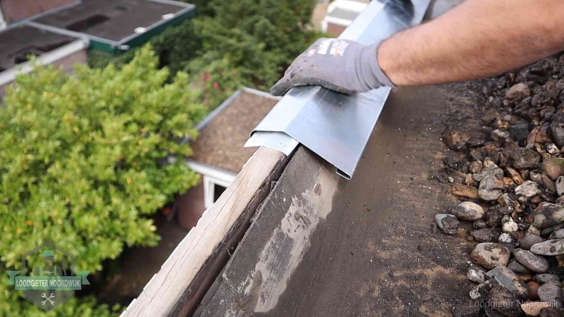 Daklekkage per wijk in Noordwijk Dakdekker plaatst een zinken deklijst op een dakrand met uitzicht over een woonwijk in Noordwijk