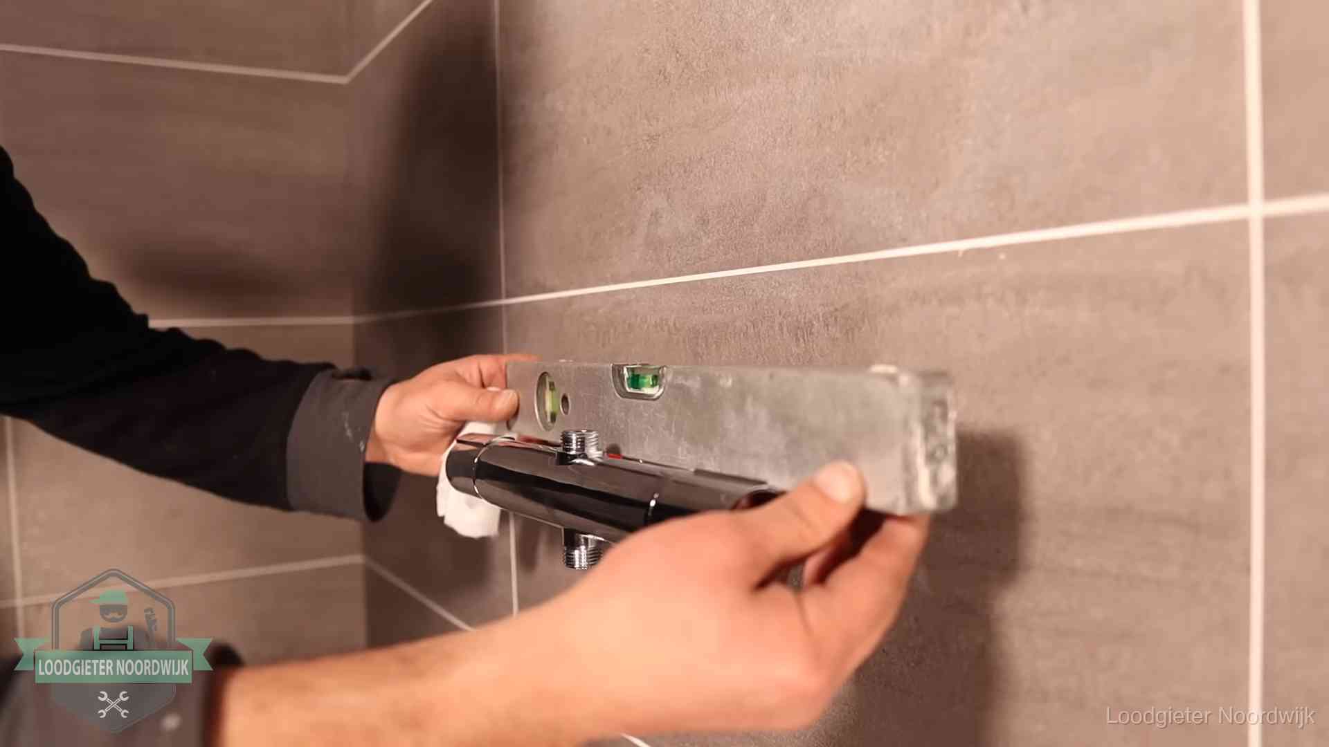 Loodgieter lijnt een douchekraan uit met een waterpas in een woning in Noordwijk