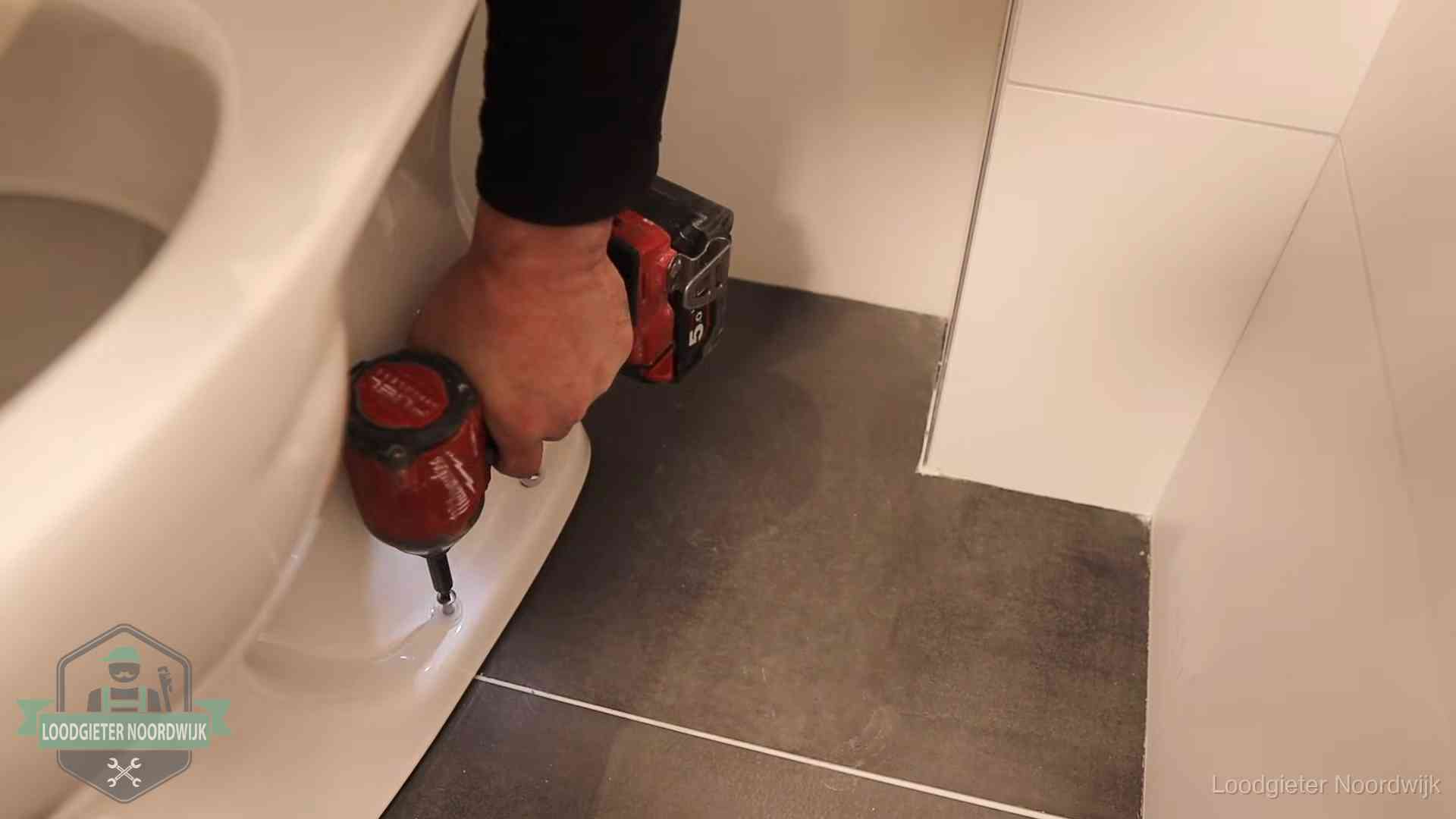 Kosten wc ontstoppen in Noordwijk Loodgieter zet de voet van een wc-pot vast op de tegelvloer in Noordwijk